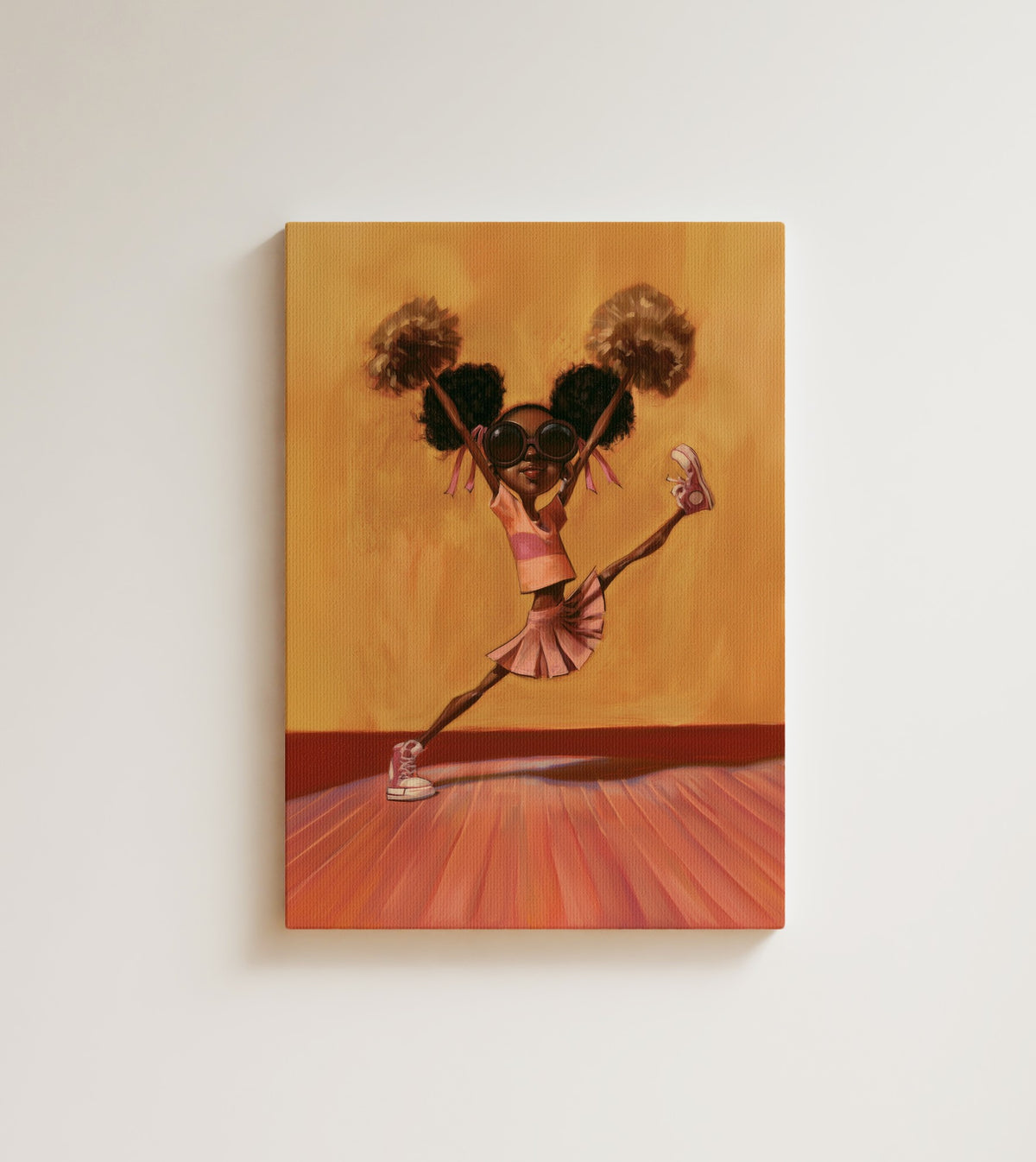 First Leap: A young Black girl jumps mid-air, pom poms high and afro puffs bouncing against a warm golden wall. Canvas wall art, shown on a plain wall