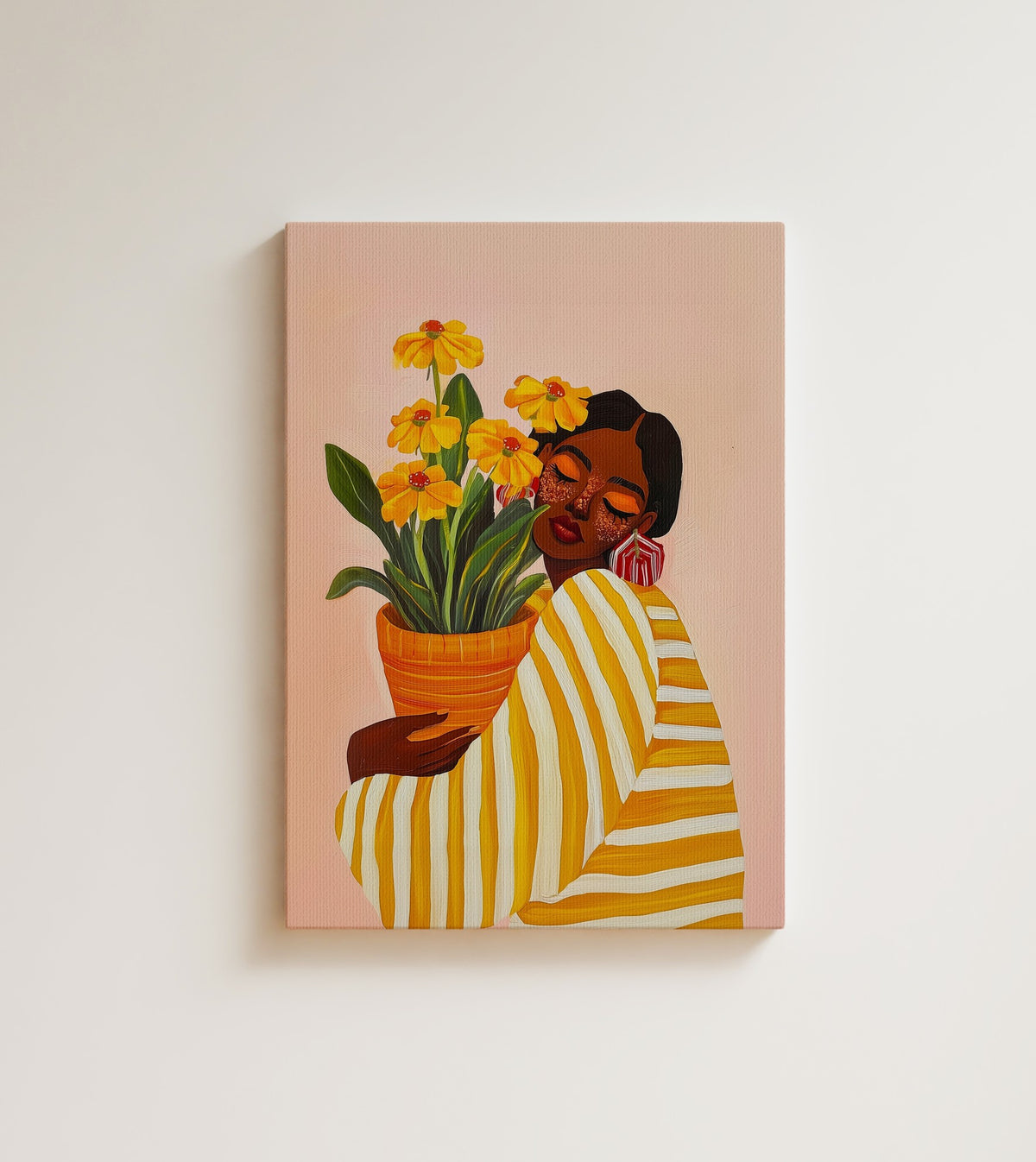 Woman with Marigolds: A woman in a yellow striped shirt hugs a pot of tall yellow daisies against a soft blush pink ground. Canvas wall art, shown on a plain wall