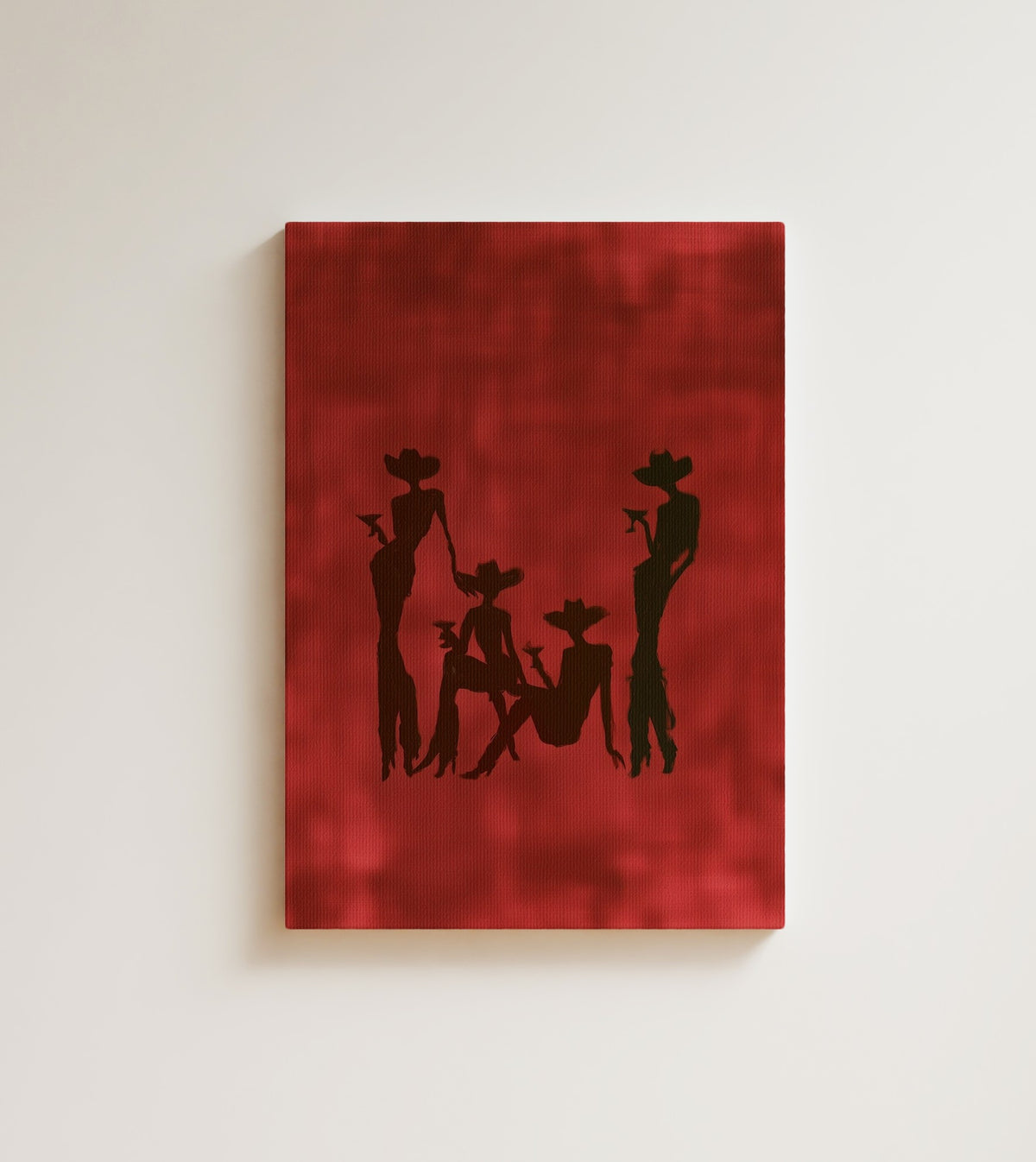 Cowgirls at Dusk: four cowgirl silhouettes raise martini glasses, brushed in near black over deep burgundy linen. Canvas wall art, shown on a plain wall