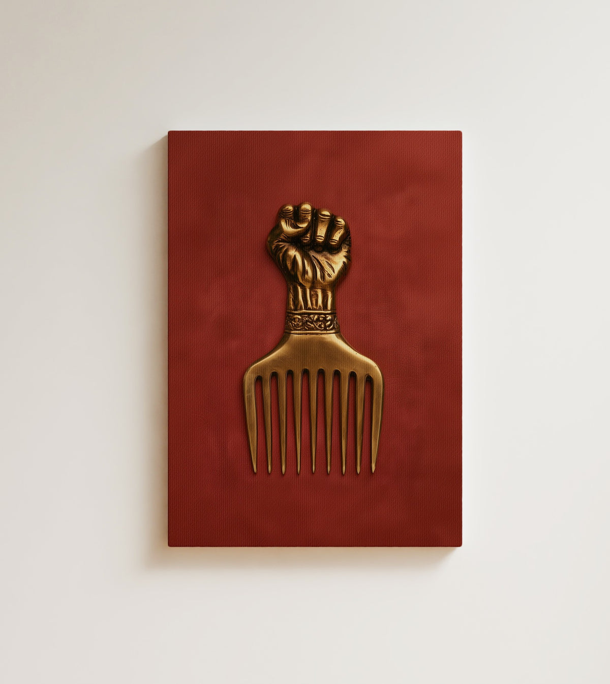 The Golden Pick: A brass afro pick with a raised fist handle stands against deep brick red. Canvas wall art, shown on a plain wall