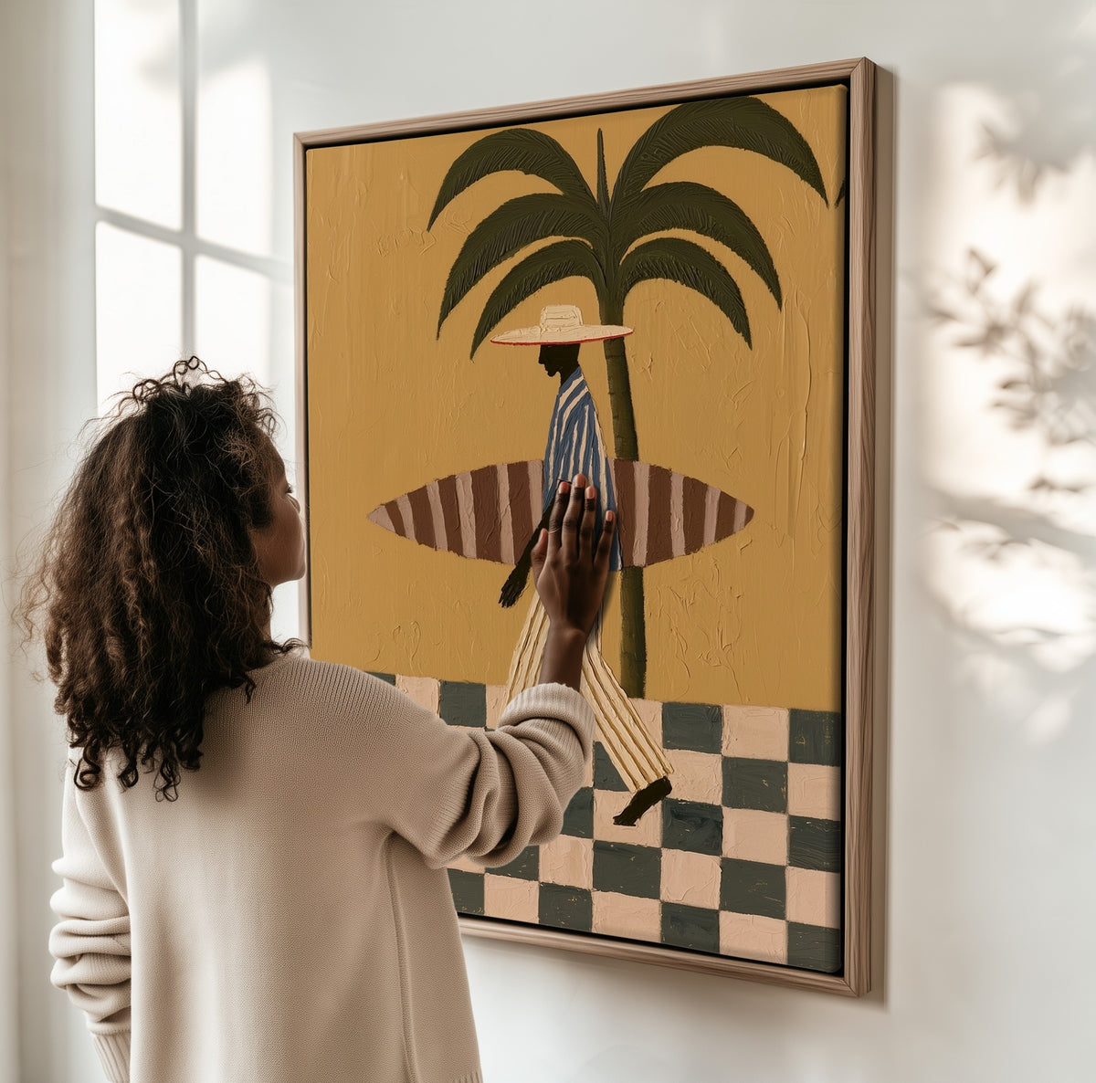 The Surfer framed canvas, a woman hanging it on a sunlit wall